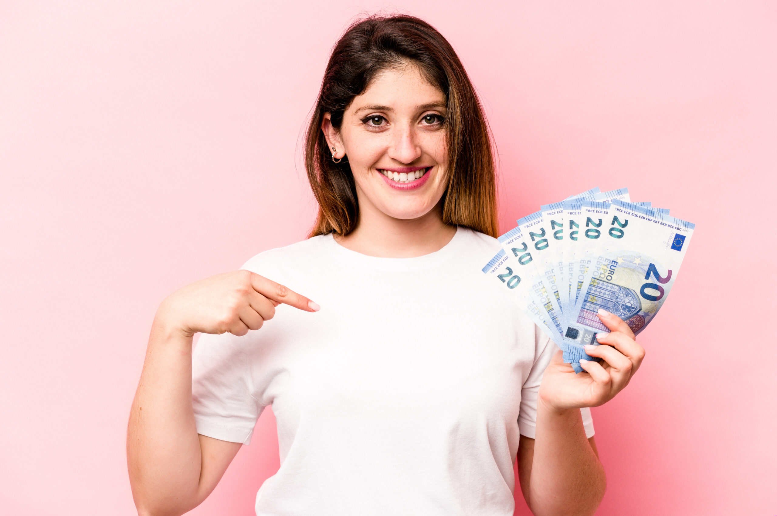 Young caucasian woman holding banknotes isolated on pink background person pointing by hand to a shirt copy space, proud and confident
